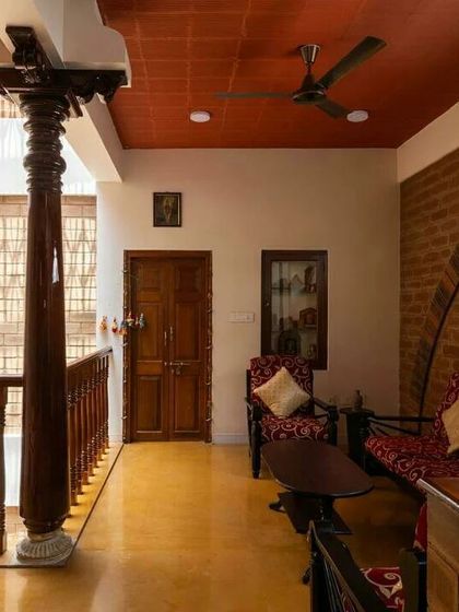An upper-level seating area defined by antique wooden pillars and railings, overlooking the floors below. The space is a modern interpretation of a traditional 'jagali' or sit-out.