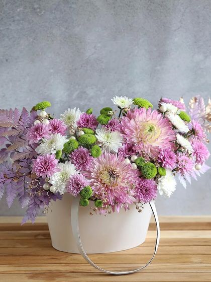 A chic arrangement of purple and white chrysanthemums in a modern white carry-bag vase, a stylish gift for any occasion.