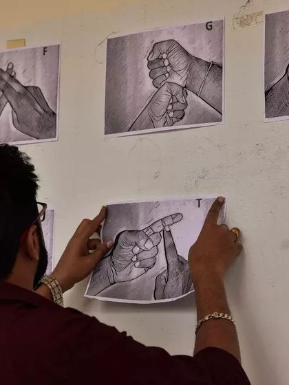 Preparing for a workshop. A volunteer puts up illustrated sign language charts on the wall, creating a visual and accessible learning environment for all participants.