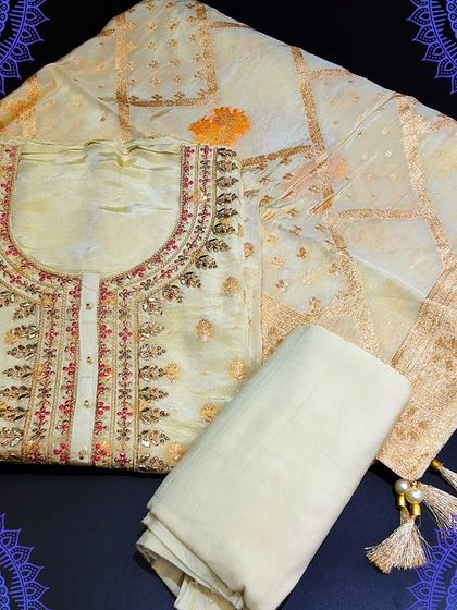 An elegant off-white unstitched suit set with delicate embroidery. It is paired with a Banarasi dupatta featuring a beautiful woven pattern and tassels.