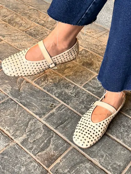 The Ecru Rivet Ballet Flats, a customer favorite, seen in action. This on-foot shot shows how the neutral color and metallic details work beautifully with classic blue jeans for an elevated casual look.