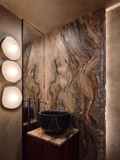 We used a dramatic, book-matched slab of exotic marble as a feature wall in this powder room. Paired with a black marble basin, it creates a powerful statement, demonstrating our use of natural materials as art.