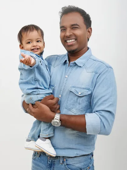 A father and son twinning in denim. This dad holds his little boy, who is pointing excitedly at something off-camera.