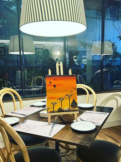 A finished painting of a sunset with telephone poles, set up on a table in a beautifully lit cafe.