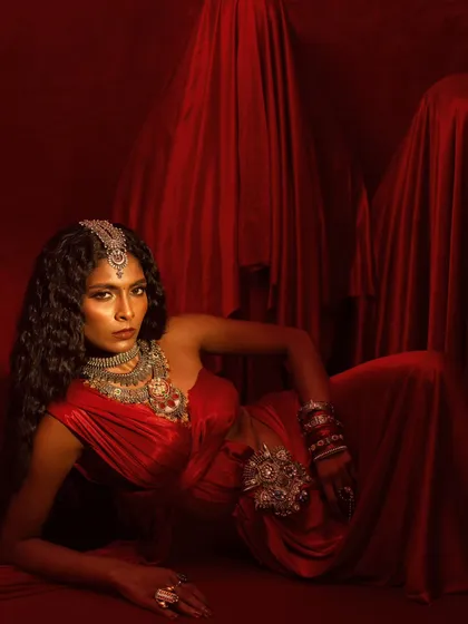 A reclining pose from the red-themed jewelry campaign. The composition allows the intricate silver jewelry to be displayed against the rich, flowing fabric.