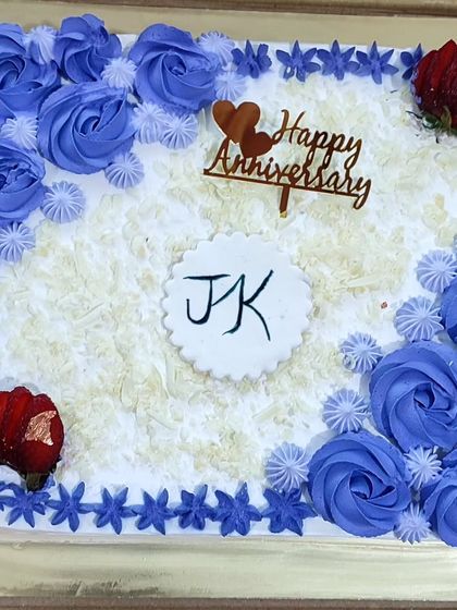 A square anniversary cake with white chocolate shavings and purple rose piping.