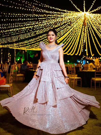For the modern bride, a glamorous reception look. This custom-designed, shimmering rose gold gown features sculpted shoulders and a tiered, flowing skirt, perfect for a cocktail party or evening celebration.