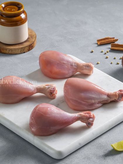 Four raw chicken drumsticks on a white marble board, a clean and minimalist shot for an e-commerce meat supplier.