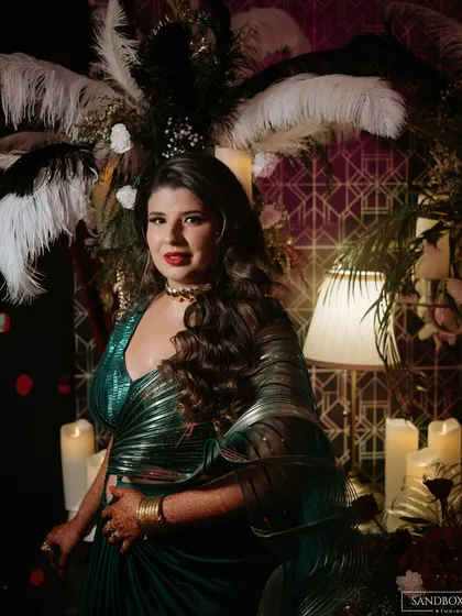 A stunning portrait of the bride in her glamorous green reception outfit, set against a backdrop of feathers and candles.