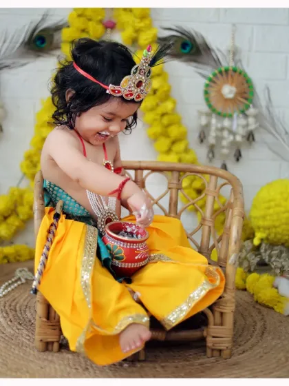 A candid shot of a little Krishna laughing while playing with a pot of 'butter'. We focus on capturing genuine, happy expressions.