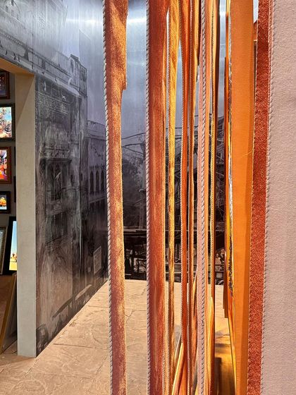 A detail from the 'Indofuturism' installation, where strips of orange fabric hang against a black-and-white image of an old Indian street. This layering of old and new, color and monochrome, augments the theme of contrasting ideas.
