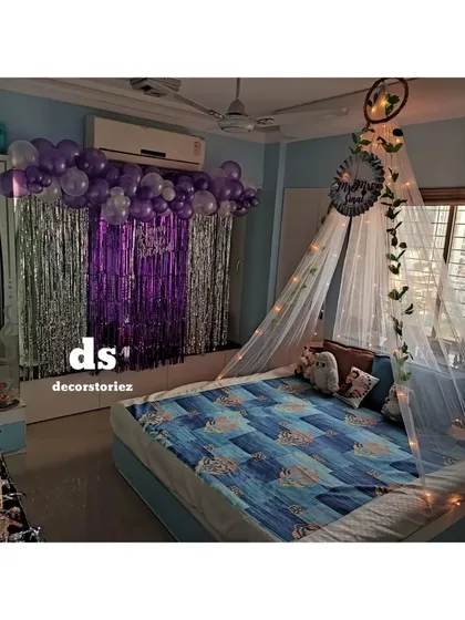 This image highlights the two main elements of the room decor: the balloon and foil curtain backdrop and the fairy light canopy over the bed, which work together to create a festive ambiance.