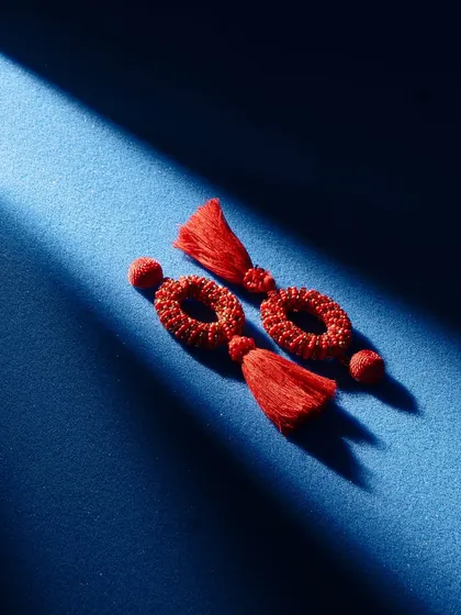 Red tassel earrings shot with dramatic, high-contrast lighting. The single sliver of light on the deep blue background creates a moody, mysterious, and very artistic image.
