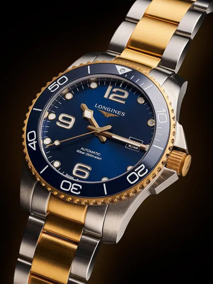 A full view of the two-tone Longines HydroConquest. This shot shows the entire watch, highlighting the interplay between the gold and steel on the bracelet and case. The lighting is designed to make the metals gleam without losing definition.