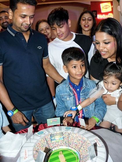 A wonderful family photo capturing the joy of the celebration around the highly detailed cricket stadium cake.