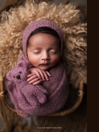 A cute little teddy bear. This newborn is snuggled up with a tiny knitted bear, adding a touch of sweetness and whimsy to the portrait.