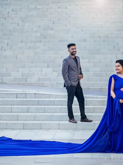 A candid moment of shared laughter against a grand, architectural backdrop. The flowing blue dress adds a touch of drama and elegance to this outdoor maternity shoot.