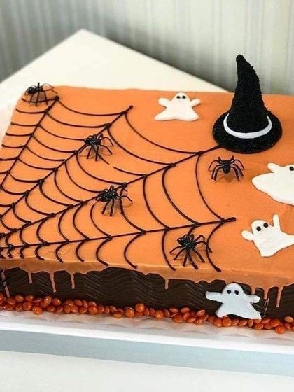 Our spooky and fun Halloween cake features a chocolate base with orange icing, complete with a spiderweb, ghosts, and a witch's hat.