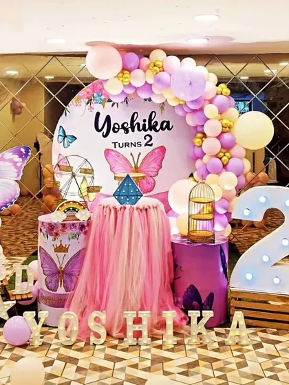 A whimsical butterfly party for a second birthday. This decoration features a circular backdrop, large butterfly props, and a marquee number '2'.