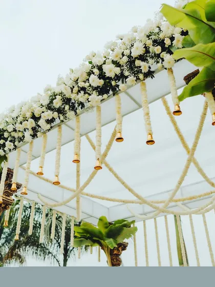 A close-up of the beautiful details on a traditional mandap, featuring hanging jasmine garlands and brass temple bells that chime with the breeze.
