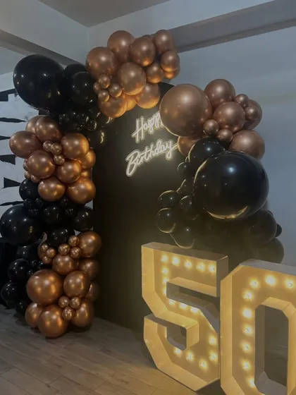 The interplay of light and shadow on this 50th birthday balloon arrangement. The neon sign and marquee lights make the metallic balloons pop, creating a dynamic visual effect.