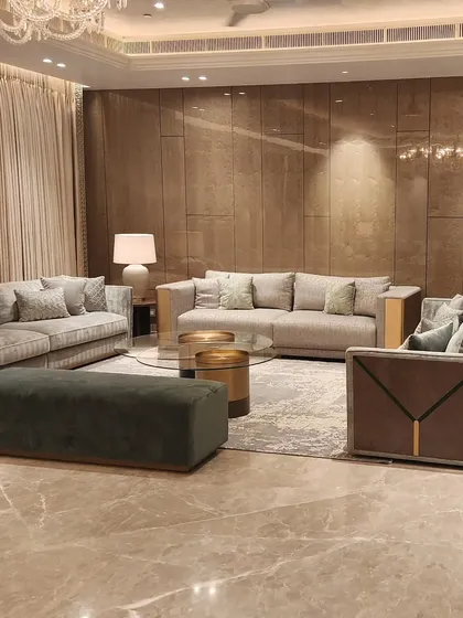 A real-life view of the Sekhri family residence at DLF Camellias. The design focuses on a warm, inviting atmosphere with plush grey sofas, a deep green ottoman, and layered textures that create a sense of quiet luxury.