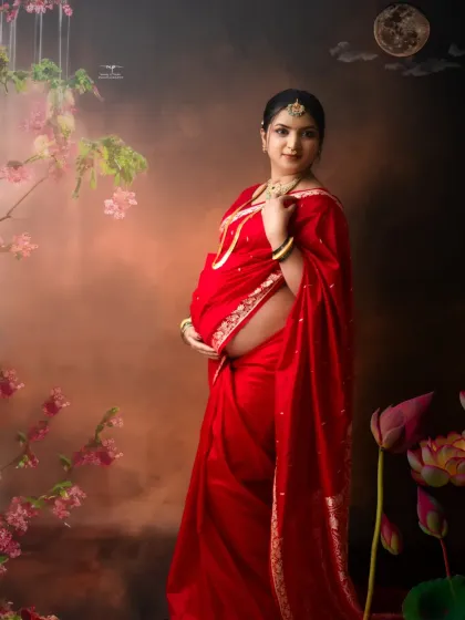 Standing tall and radiant, this mother-to-be is framed by a dreamy, painterly background with lotus flowers, adding to the artistic and traditional feel of the portrait.