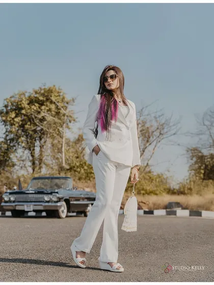 A confident and stylish portrait of the bride-to-be in a white suit with a vintage car in the background. This shot has a strong, independent, and fashionable feel.