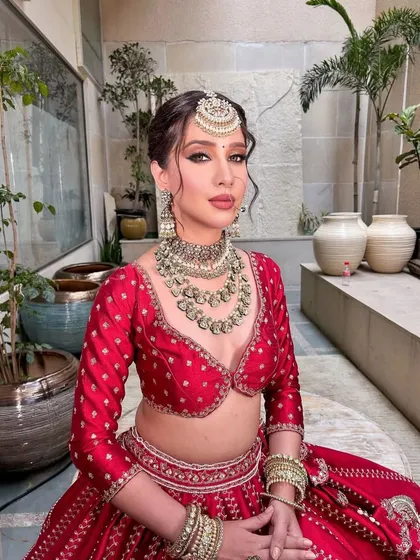 A serene portrait of a bride in red. The styling is classic and elegant, with a focus on the beautiful jewelry and the rich color of the lehenga.