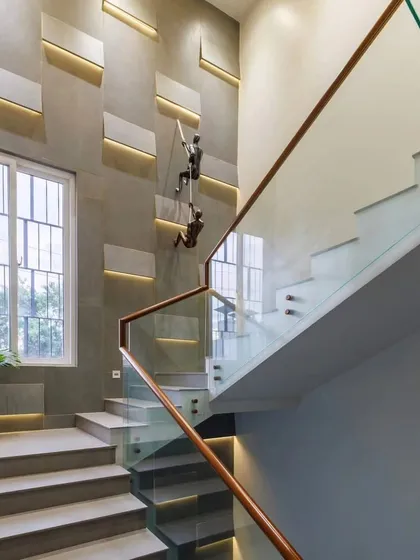 We transformed this duplex staircase into a striking design feature. The wall is clad in textured concrete panels with integrated backlighting, creating a dramatic play of light and shadow. A glass railing with a wooden handrail ensures safety while maintaining an open, airy feel, complemented by unique climbing-figure art pieces that add a touch of whimsy.