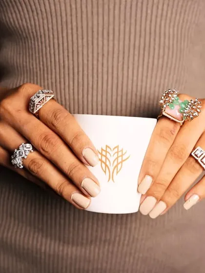 A lifestyle shot of a model holding a cup, her hands adorned with a variety of our statement rings, showing how they can be styled for everyday luxury.