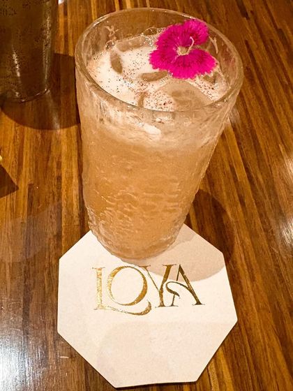 A close up of a flavor forward cocktail from Loya's 'Vriksh' menu. The floral garnish and custom coaster are the kind of details that elevate a drink and make for great content.