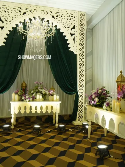 A photo corner with an ornate white arch, deep green velvet curtains, and a crystal chandelier, creating a look of royal elegance.