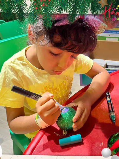 A young boy is focused on personalizing a glittery green bauble for his Christmas tree. Our DIY craft stations are a great way for kids to create their own holiday decorations.
