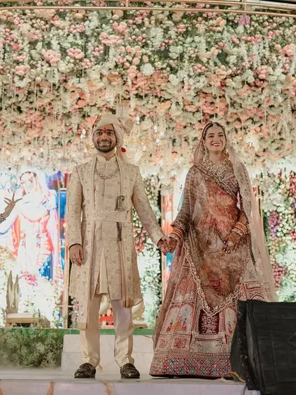 The couple stands hand-in-hand on the grand Varmala stage. The combination of a floral canopy, divine digital backdrop, and live performers creates a multi-layered, unforgettable experience.
