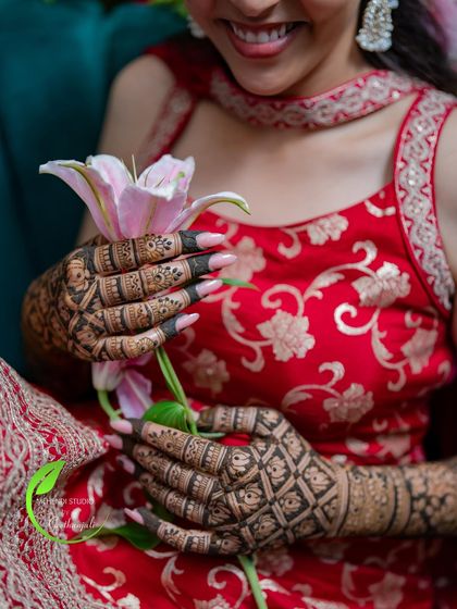 A close-up shot of the bride's hands holding a lily, showcasing the beautiful jaali (net) pattern on her mehendi.
