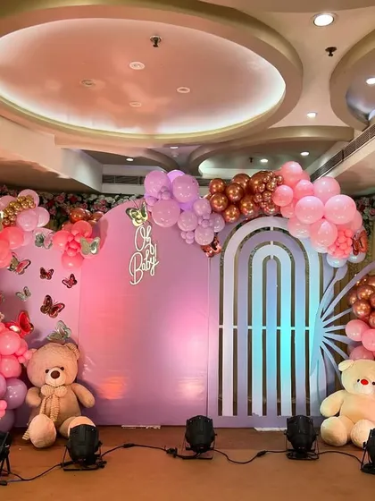 A grand 'Oh Baby' shower with a butterfly theme. This stage features a large pastel purple backdrop, butterfly wing-shaped balloon arrangements, and cute teddy bears for a whimsical touch.