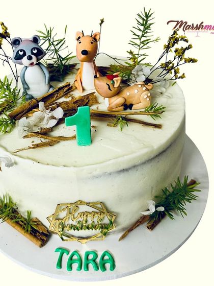 Celebrating a first birthday with a cozy winter woodland theme. This cake features adorable, hand-sculpted fondant animals like a raccoon and deer, nestled among rustic, edible details.