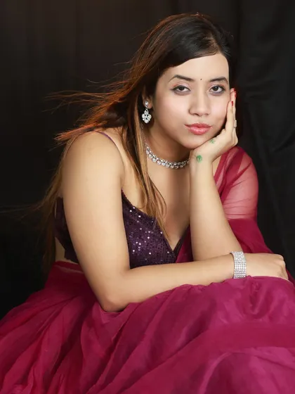 A simple, elegant seated portrait against a black studio backdrop. The lighting is soft and focused on the model's face, creating a classic beauty shot.