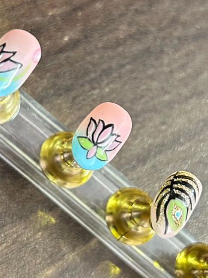 A close-up on the intricate line work of the lotus and peacock feather nail art. Every detail is painted with a fine brush to achieve a clean and beautiful result.
