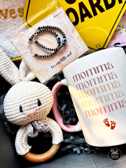 A sweet and simple hamper for a new mom and baby, featuring a 'Momma' mug, a crochet bunny rattle, and a traditional nazariya bracelet to protect the little one.