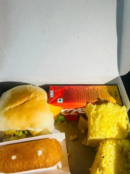A simple yet satisfying snack box option featuring a classic vada pav, soft dhokla, a sweet cake, and a juice box. These are ideal for quick distribution at events or as a travel snack.