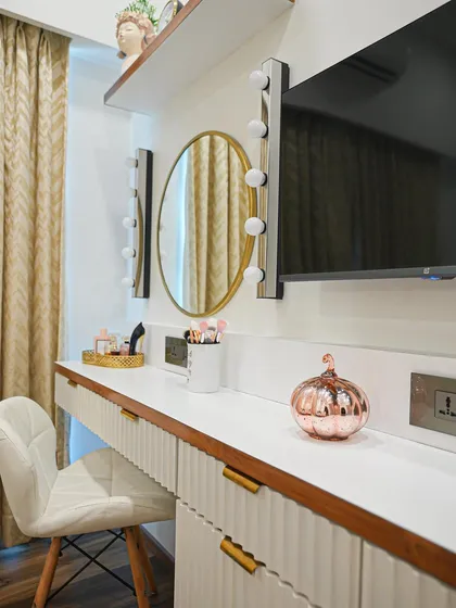 The vanity area in the master bedroom features a sleek white dresser with fluted details, a round mirror, and classic makeup lights for a touch of Hollywood glamour.