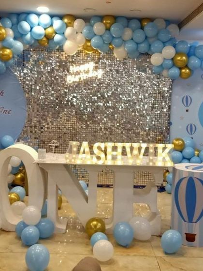 A 'Fly High Little One' theme featuring a silver shimmer wall, hot air balloon props, and a massive balloon arch in shades of blue and white.