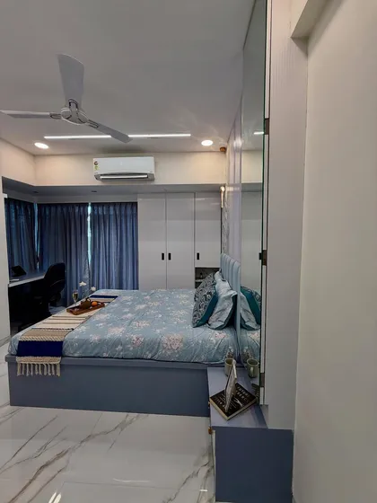 A full view of a master bedroom with a cool blue color scheme, floor-to-ceiling wardrobes, and an integrated study or dressing table. The mirrored wardrobe panels make the room feel larger.