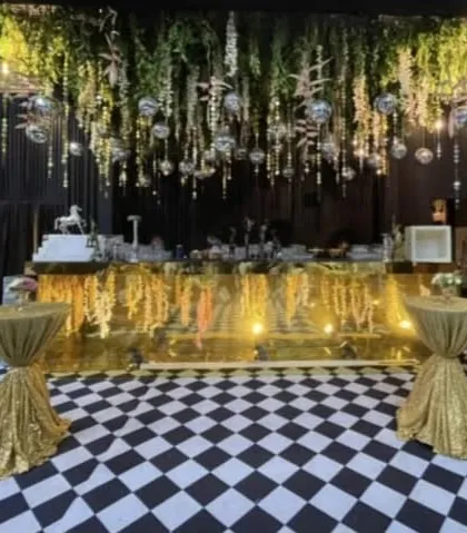 A glamorous bar and lounge area with a checkered floor, a reflective gold bar front, and an overhead installation of hanging greenery and disco balls. This setup is perfect for a high energy product launch or a celebratory cocktail party.