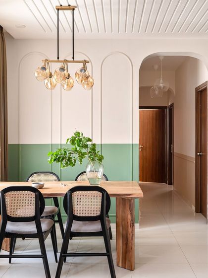 This dining corner features a two-tone wall with sage green paint and arched beadings, creating a sophisticated backdrop. The wooden table, wicker-back chairs, and a statement chandelier complete this elegant and modern dining space.
