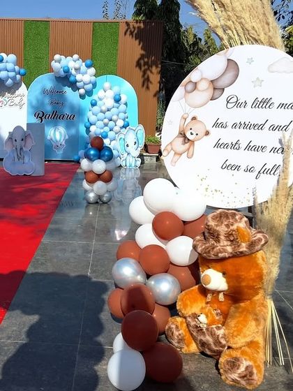 A personalized welcome sign for a baby boy's party, featuring a cute teddy bear and a heartfelt message, placed next to a beautiful balloon arrangement.