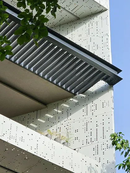 A detail shot of the builder floor in Gurugram, focusing on the perforated aluminum jali and the sleek aluminum louvers. The play of light and shadow through the perforations adds a dynamic quality.
