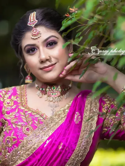 A close-up portrait of a bride with a pink saree, taken outdoors. The makeup is soft and natural, perfect for daytime.